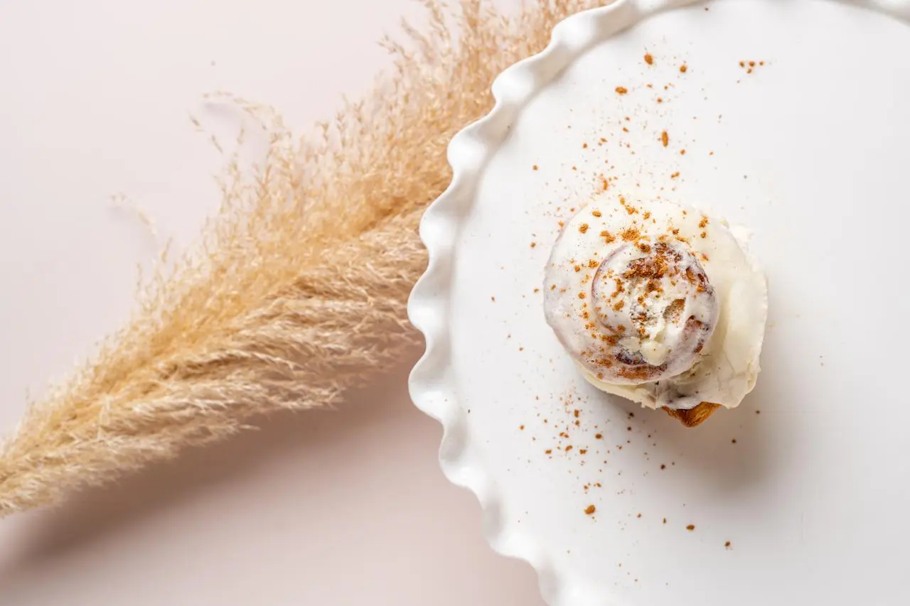 Cream topped sweet roll beside dried pampas grass
